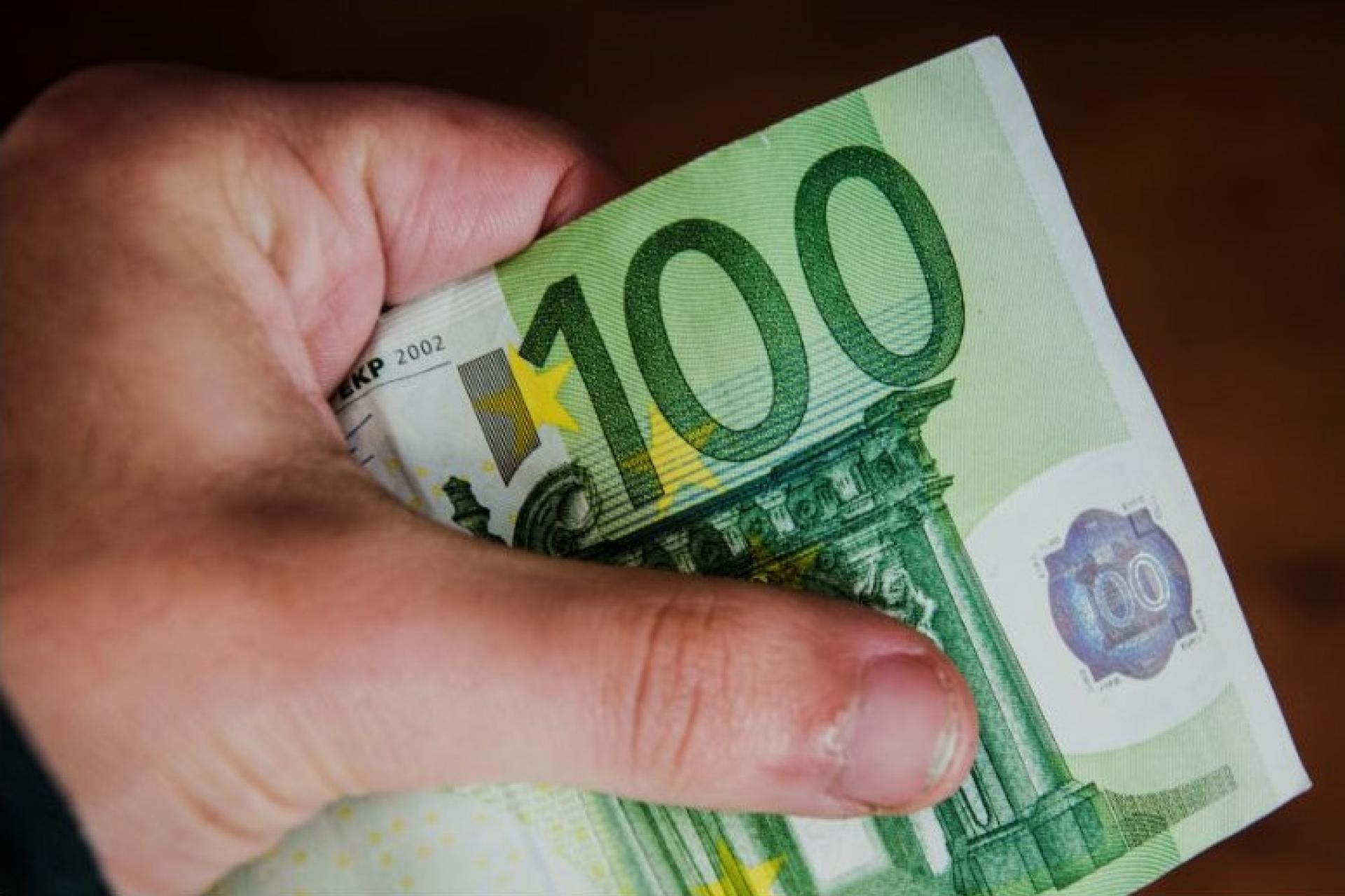 Iemand houdt in zijn hand een briefje van 100 euro vast