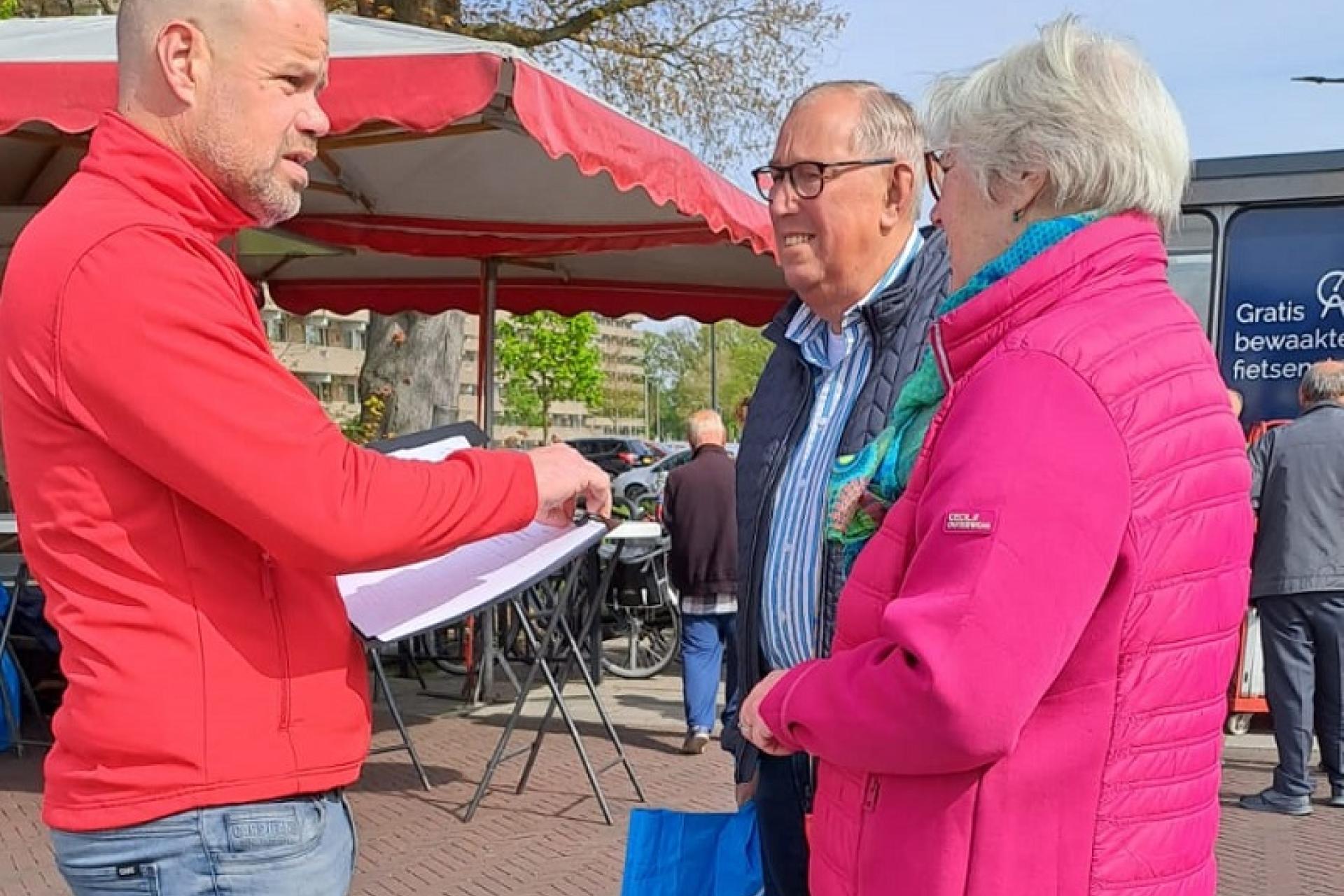 Wethouder Niels van den Berg in gesprek met 2 inwoners op de markt in Enschede Zuid
